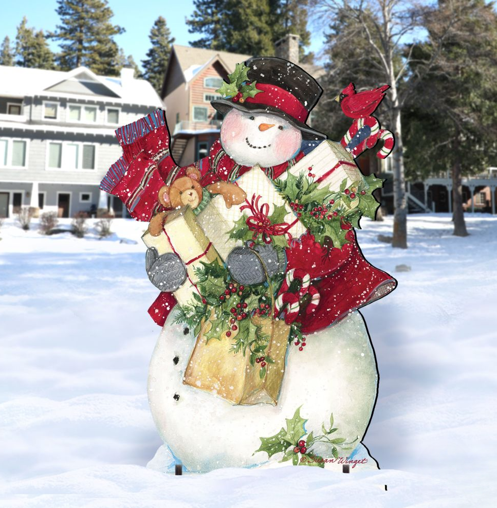 A snowman figure holding presents and a teddy bear stands in the snow, with a house and trees in the background.