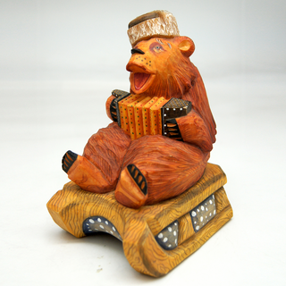 A wooden figurine of a bear sitting on a wooden base and playing an accordion.