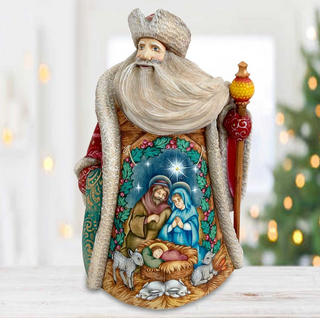 A figurine of Santa Claus holding a nativity scene with a baby Jesus and Mary, surrounded by animals, is displayed on a table with a blurred background of a Christmas tree.