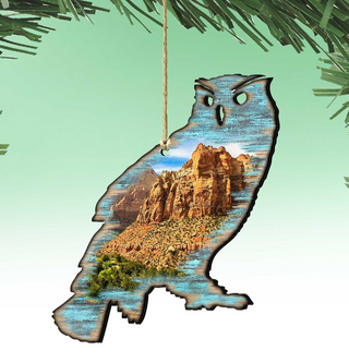 A wooden ornament in the shape of an owl, with a landscape scene inside its body, hanging against a green background.