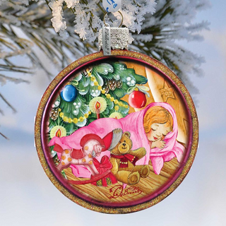 A round Christmas ornament with a painting of a sleeping girl and a teddy bear.