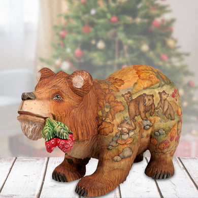 A wooden bear figurine with a painted design of bears and berries, placed on a wooden surface in front of a blurred Christmas tree.