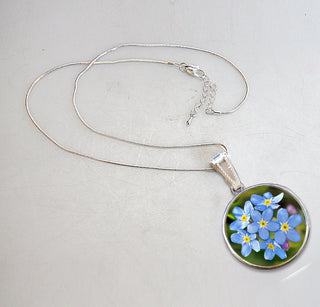 A silver necklace with a pendant featuring a circular design of blue forget-me-not flowers.