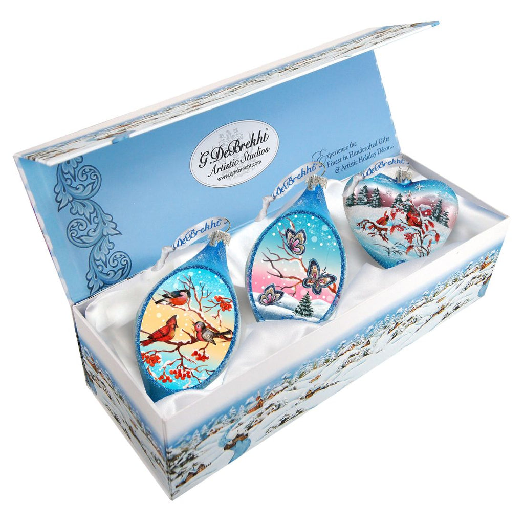 A set of three ornaments in a blue box, each with a unique design, including a bird, butterflies, and snowflakes.