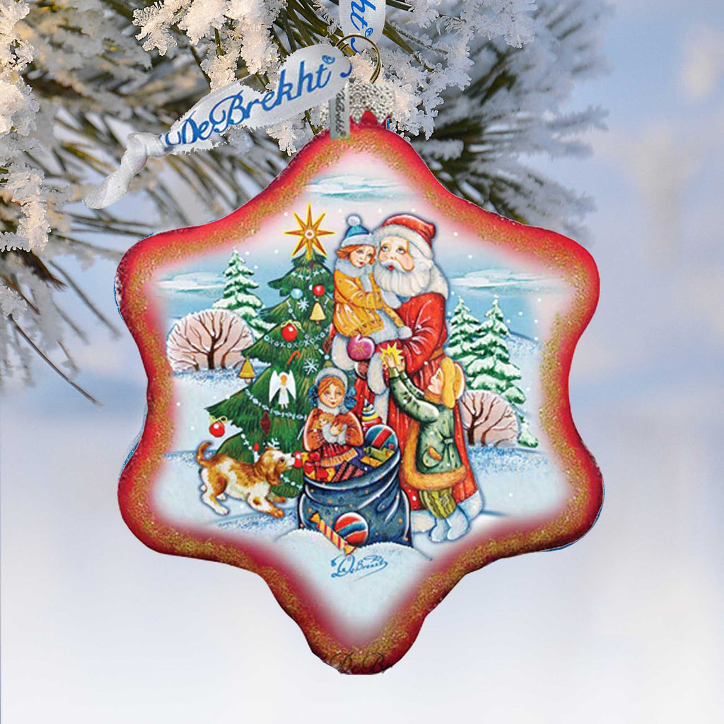 A red star-shaped ornament with a Christmas tree and Santa Claus figures, along with other holiday-themed elements, hangs from a tree branch.