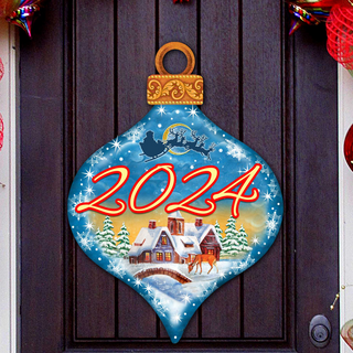A blue ornament with a snowy village scene and a Santa Claus sleigh is hanging on a door.