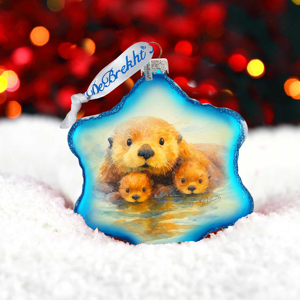 A blue star-shaped ornament with a painting of a brown otter and its two young otters in the center, set against a background of red and orange lights.