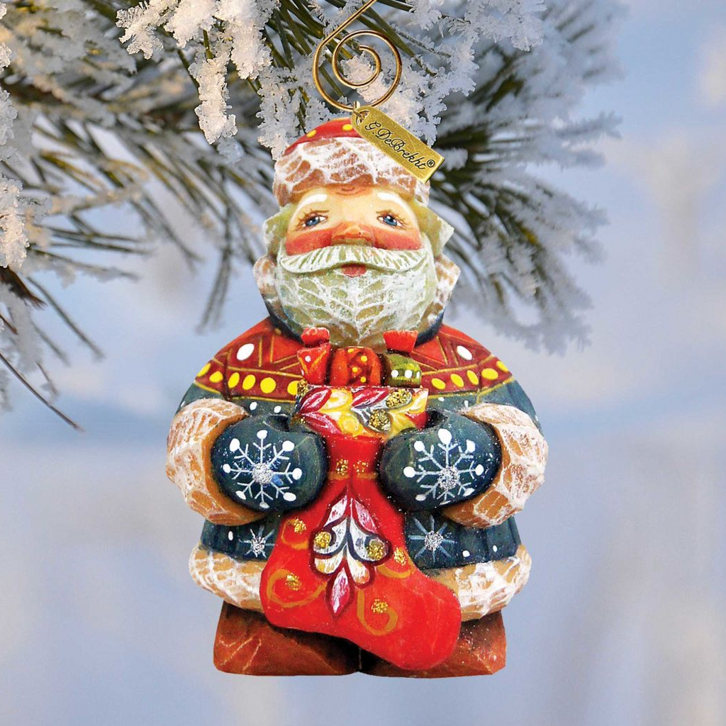 A colorful ornament of Santa Claus hanging on a tree branch, with snow on the branches.