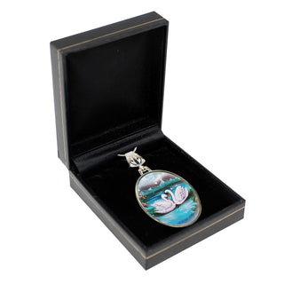 A pendant in a black jewelry box, featuring a design of two swans swimming in a pond.