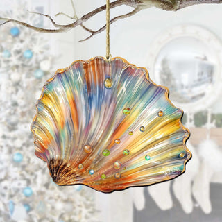 A colorful glass ornament resembling a seashell hangs from a branch, with a blurred background that includes a Christmas tree and a mirror.