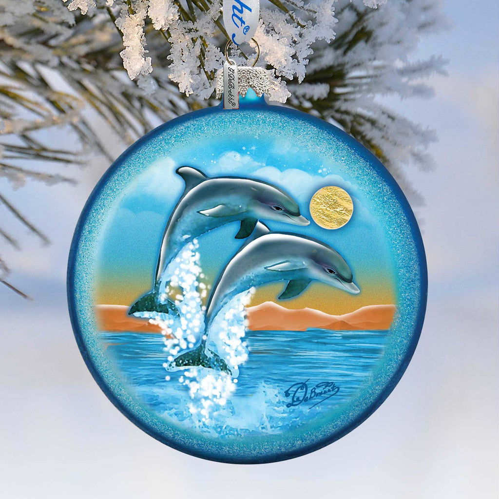 A blue ornament with a painting of two dolphins leaping out of the water, set against a snowy background.