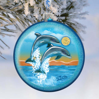 A blue ornament with a painting of two dolphins leaping out of the water, set against a snowy background.