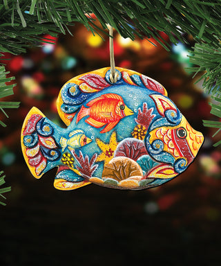 A colorful, hand-painted ornament in the shape of a fish hangs from a tree branch, surrounded by greenery.