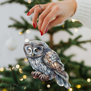 a hand holding an owl ornament on a christmas tree
