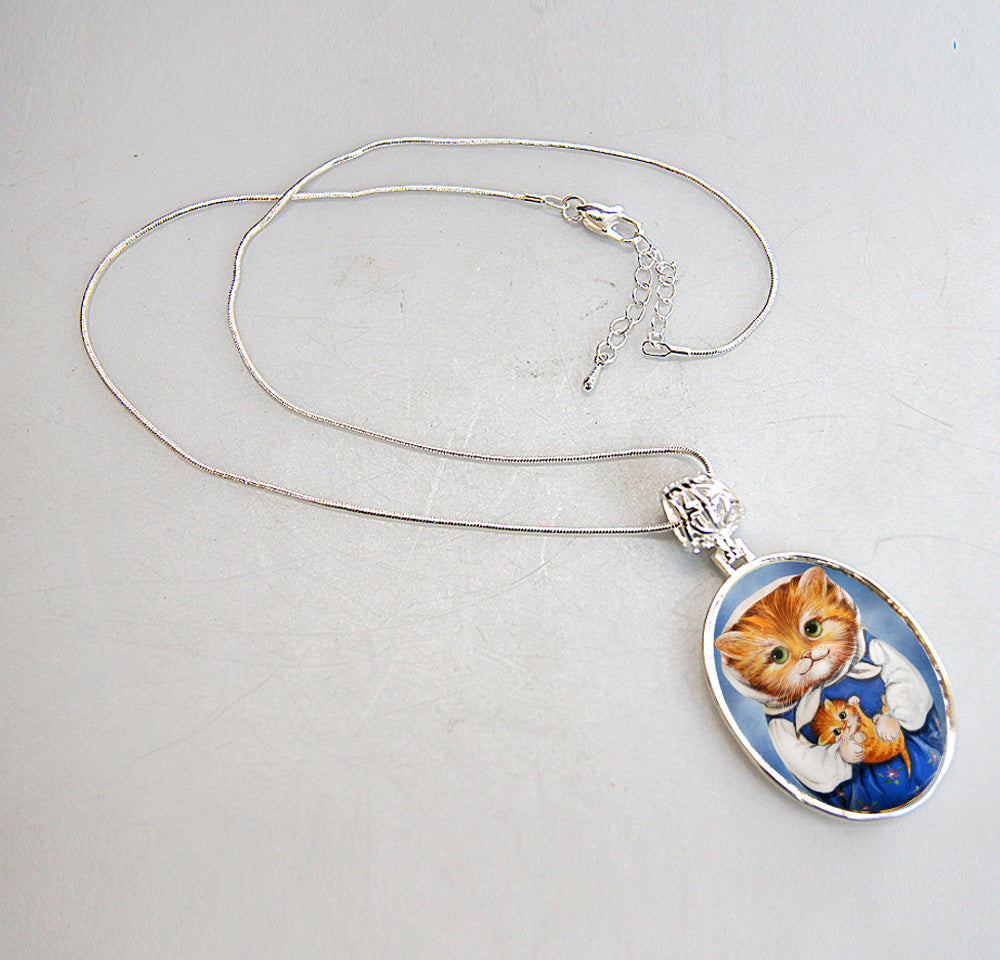 A silver necklace with a pendant featuring a painting of two cats, one larger and one smaller, wearing blue outfits.