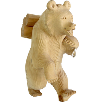A wooden bear sculpture with a backpack on its back, standing upright and carrying a large log.