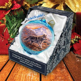 A blue and white ornament in a box, featuring a wolf in a snowy landscape, surrounded by holiday decorations.