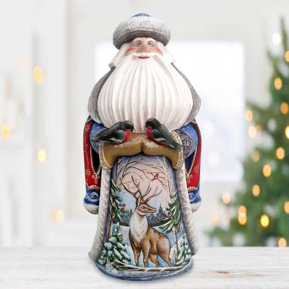 A figurine of Santa Claus sitting on a snowy landscape, with a deer and birds in the background.