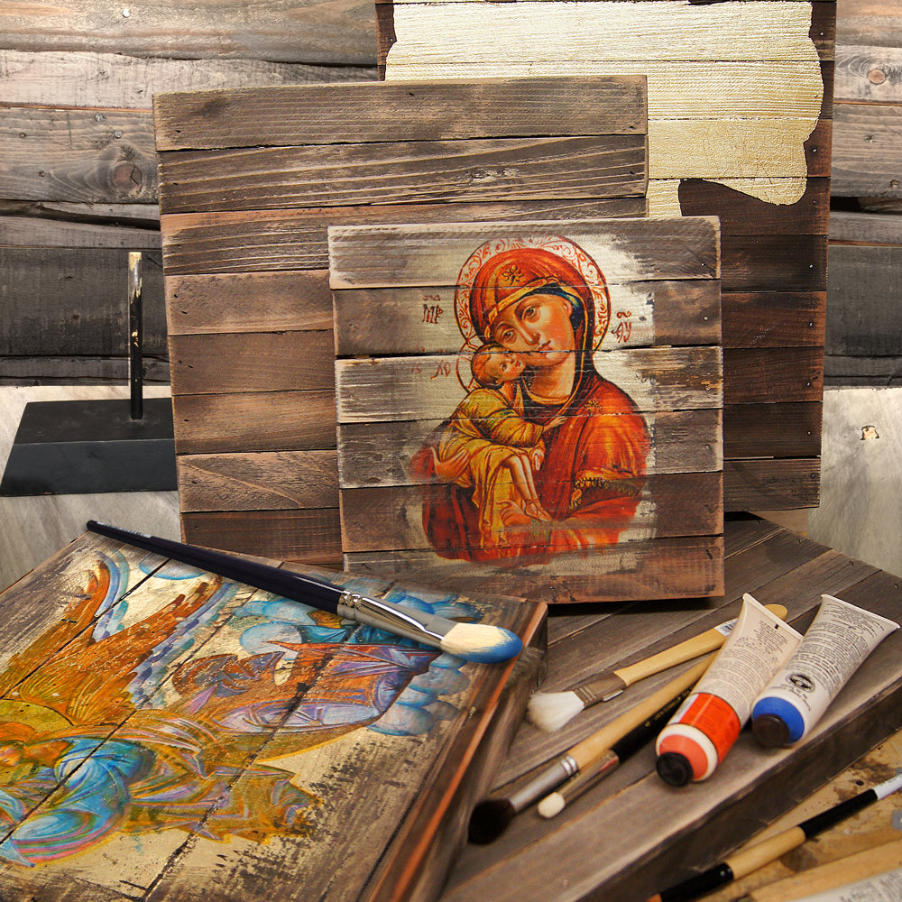 a wooden frame with a painting of the Virgin Mary and baby Jesus, surrounded by art supplies such as paintbrushes and tubes of paint.