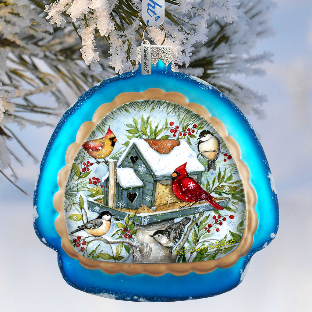 A blue ornament with a winter scene featuring a birdhouse, red cardinal, and other birds, surrounded by snow and greenery.