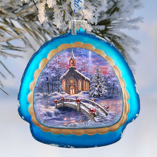 A blue ornament with a winter scene depicting a church, a bridge, and snow-covered trees.