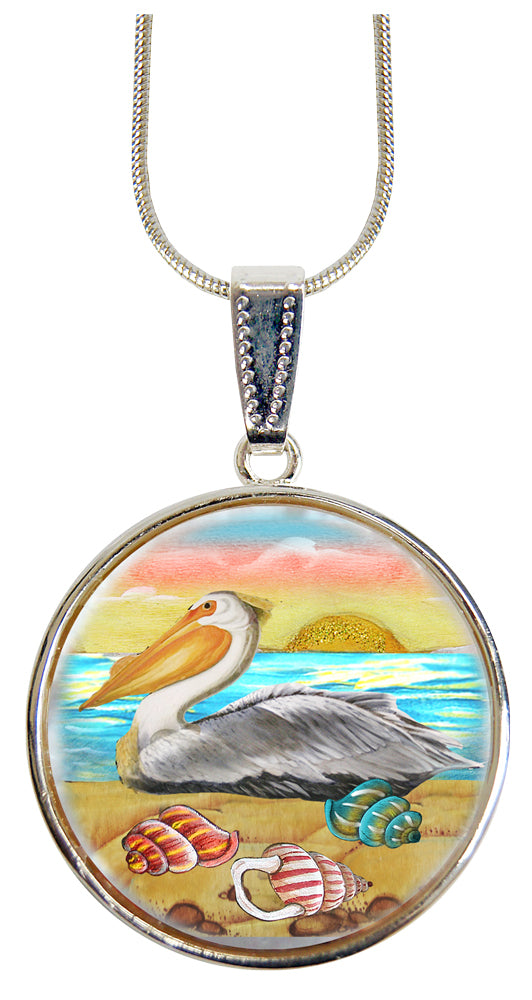 A pendant necklace with a circular design featuring a pelican, a sunset, and various seashells.
