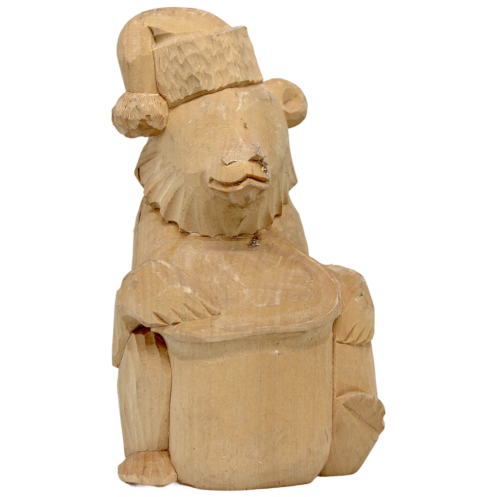 A wooden carving of a bear wearing a hat and holding a drum.