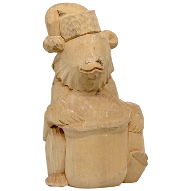 A wooden carving of a bear wearing a hat and holding a drum.