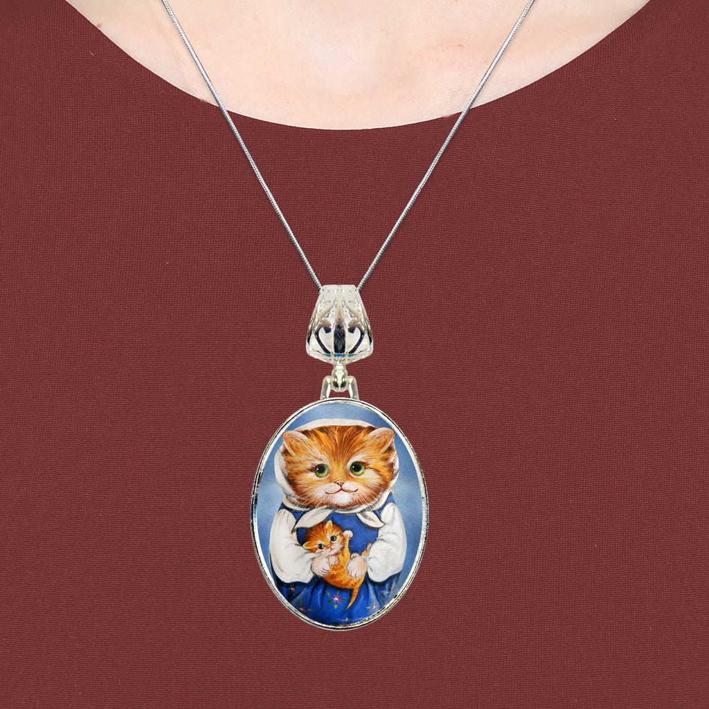 A silver necklace with a pendant featuring a painting of a cat wearing a blue dress.