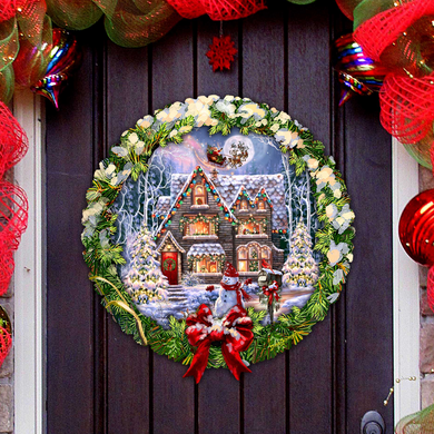 A wreath with a Christmas scene on it, featuring a snowy house, trees, and a Santa Claus figure.