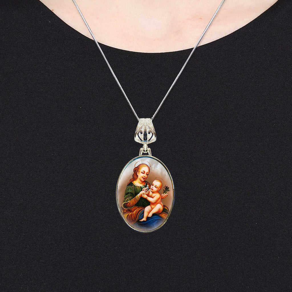 A silver necklace with a pendant featuring a painting of a woman holding a baby.