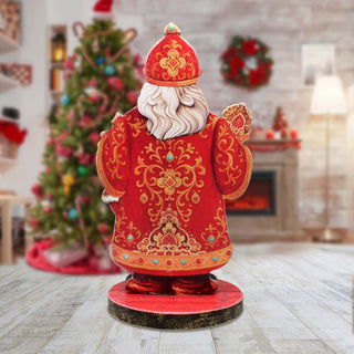 A red and gold Christmas-themed statue of Santa Claus stands on a wooden base in a room decorated for the holiday season.