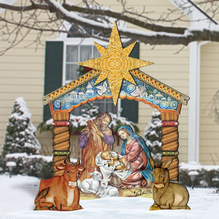 A large, colorful, and detailed cardboard nativity scene depicting the birth of Jesus Christ, with figures of the Virgin Mary, baby Jesus, and other figures arranged in a manger. The scene is set against a snowy background, with a house and trees visible in the distance.