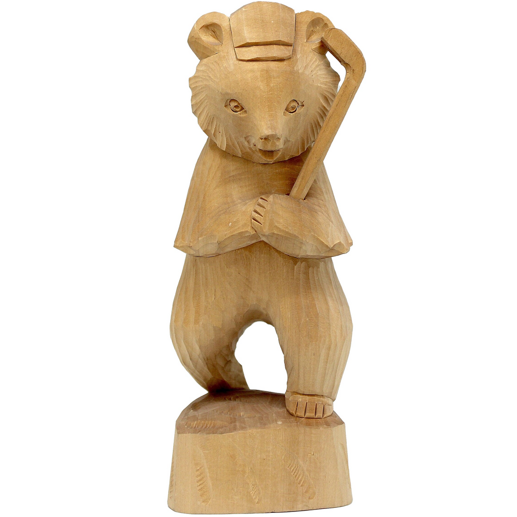 A wooden carving of a bear standing on one leg, wearing a hat and holding a cane.