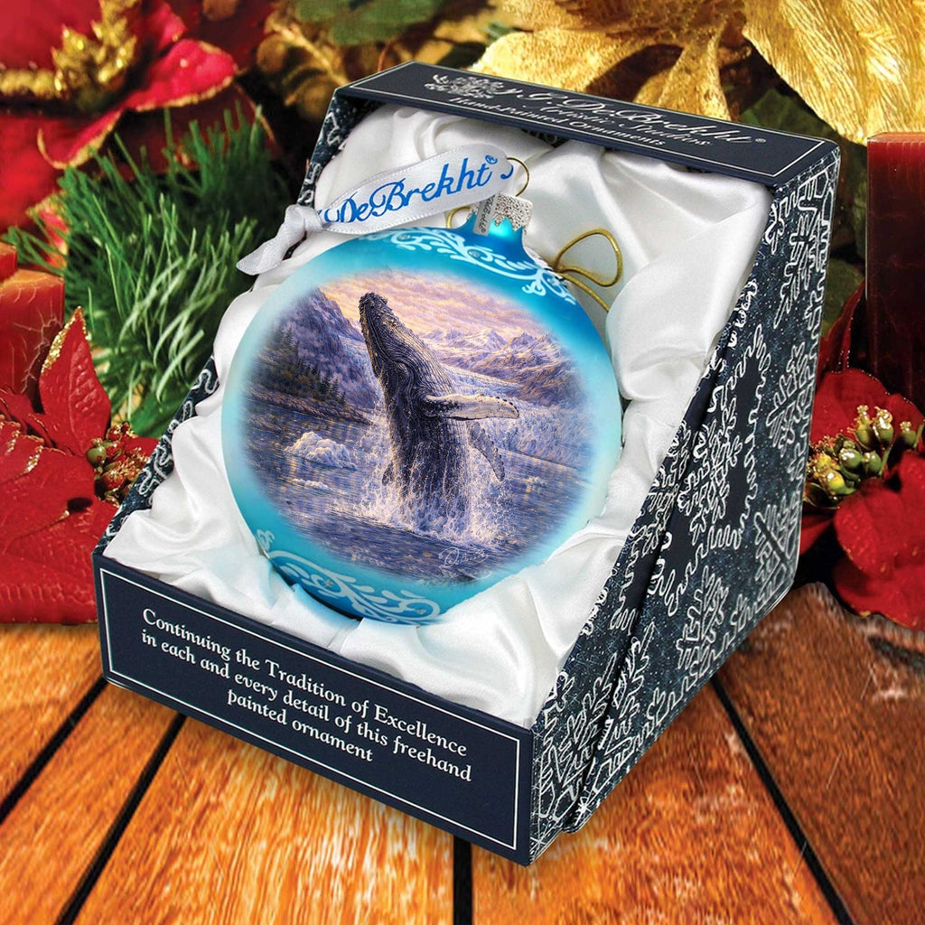 A blue and white ornament in a box, featuring a whale in a snowy landscape, surrounded by holiday decorations.