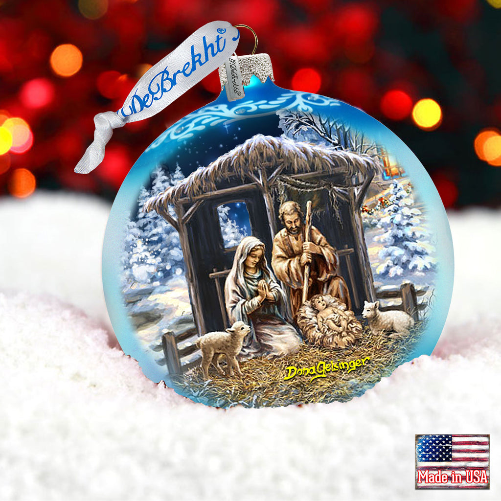 A blue Christmas ornament with a nativity scene depicting the birth of Jesus Christ, featuring the Virgin Mary, baby Jesus, and other figures in a snowy landscape.