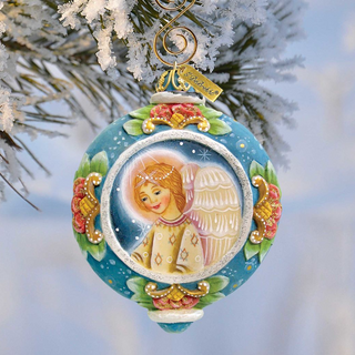 A blue Christmas ornament with a painted angel figure is hanging from a tree branch.