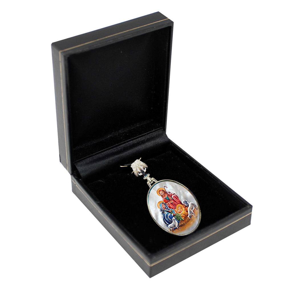 A round pendant with a religious scene is displayed in a black jewelry box.