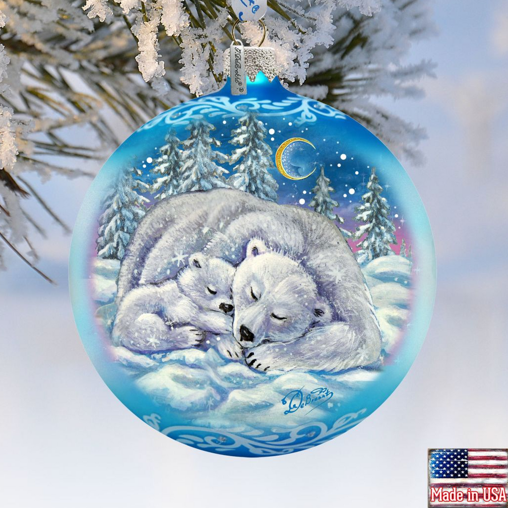 A blue Christmas ornament with a painting of a mother polar bear and her cub resting in the snow, with a crescent moon and stars in the night sky.