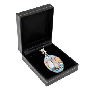 A pendant with a sailboat design is displayed in a black jewelry box.