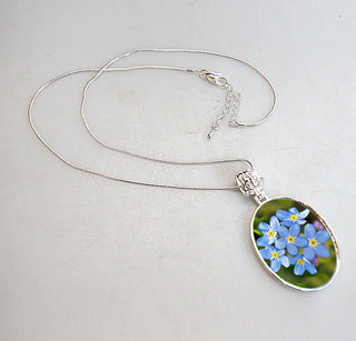 A silver necklace with a pendant featuring a close-up image of blue forget-me-not flowers.