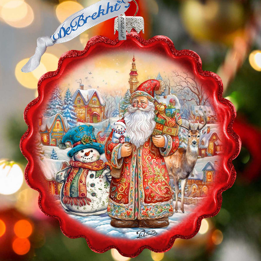 A red ornament with a snowy village scene featuring Santa Claus, a snowman, and reindeer.