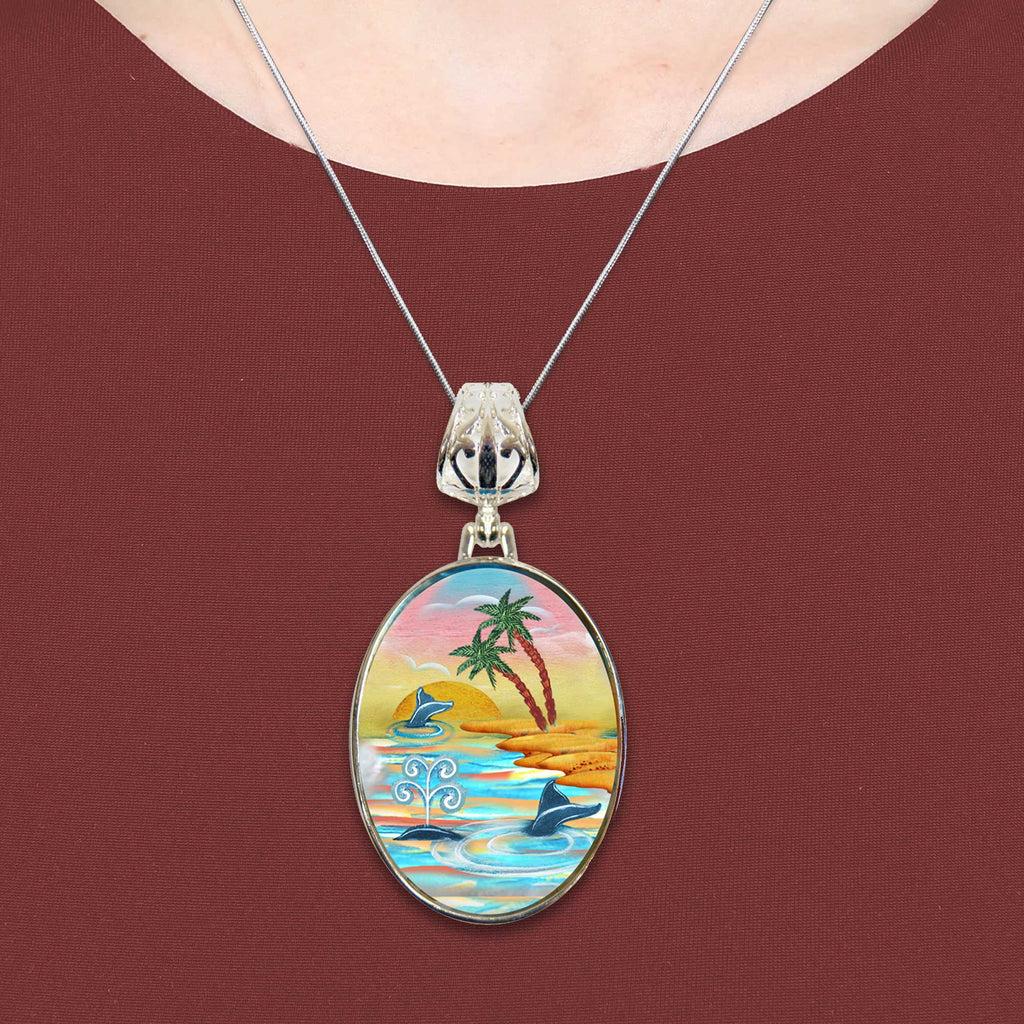 A necklace with a pendant featuring a colorful tropical scene with palm trees, a sunset, and a body of water.