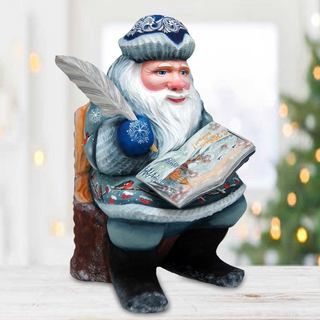 A figurine of Santa Claus sitting in a chair and reading a book, with a feather quill in his hand.