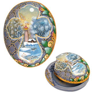 a decorative oval-shaped object with a winter landscape scene, including a lighthouse, trees, and a body of water.
