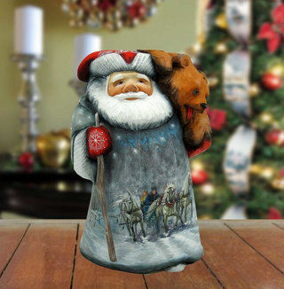 A figurine of Santa Claus holding a teddy bear, with a snowy winter scene depicted on the Santa's suit.