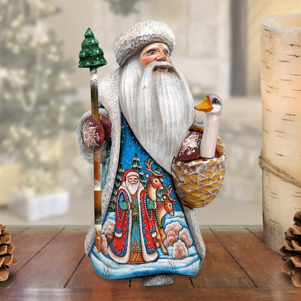 A colorful, handcrafted Santa Claus figurine holding a basket of reindeer and a Christmas tree, standing on a wooden surface.