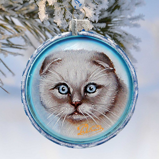 A blue ornament with a picture of a cat's face on it, hanging on a snowy branch.