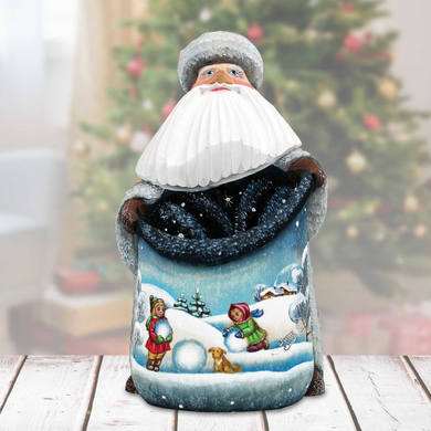 A figurine of Santa Claus holding a bag with a winter scene depicted on it, set against a blurred background of a Christmas tree.