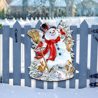 A snowman decoration with a red scarf, black top hat, and various animals, including a bird, is displayed on a blue picket fence in a snowy landscape.